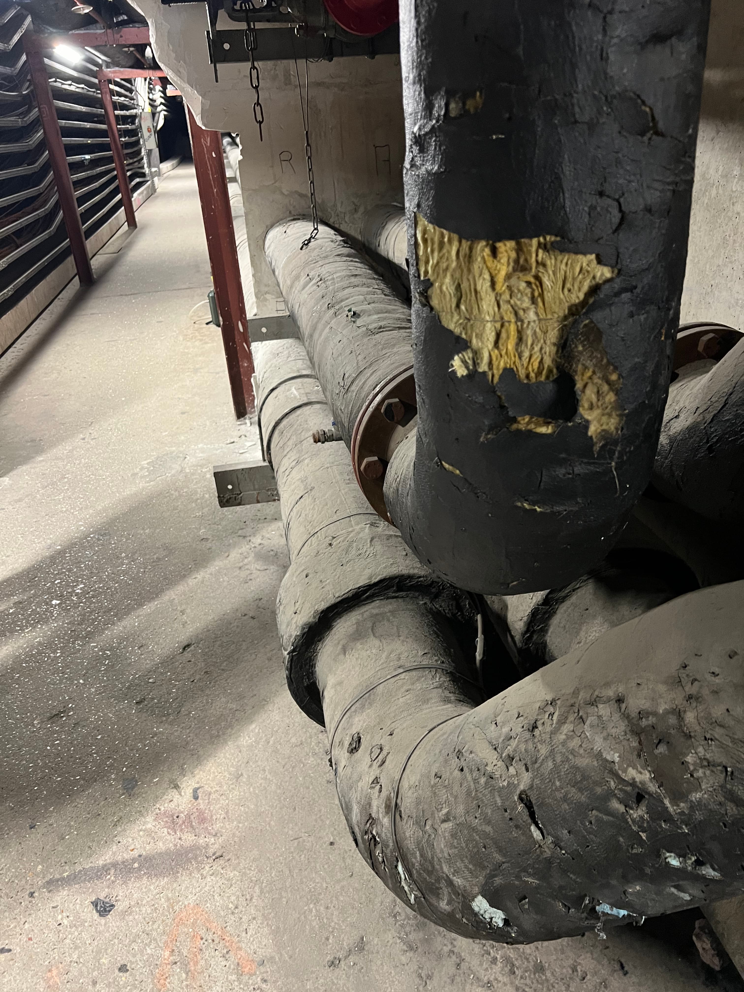 Gros plan sur un coude de tuyauterie présentant un isolant thermique déchiré, causant des ponts thermiques avant l'intervention.