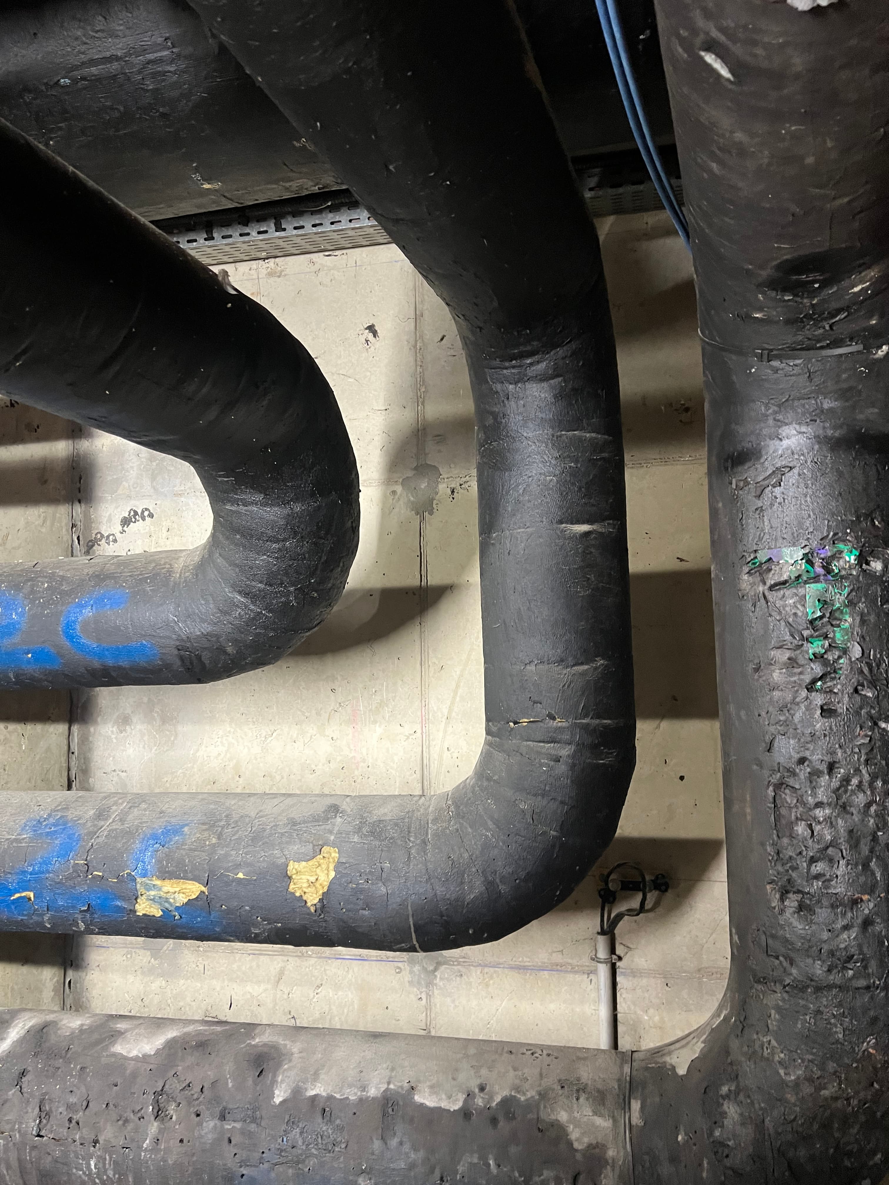Vue complexe de réseaux de tuyauteries superposées nécessitant une rénovation complète de leur protection mécanique.